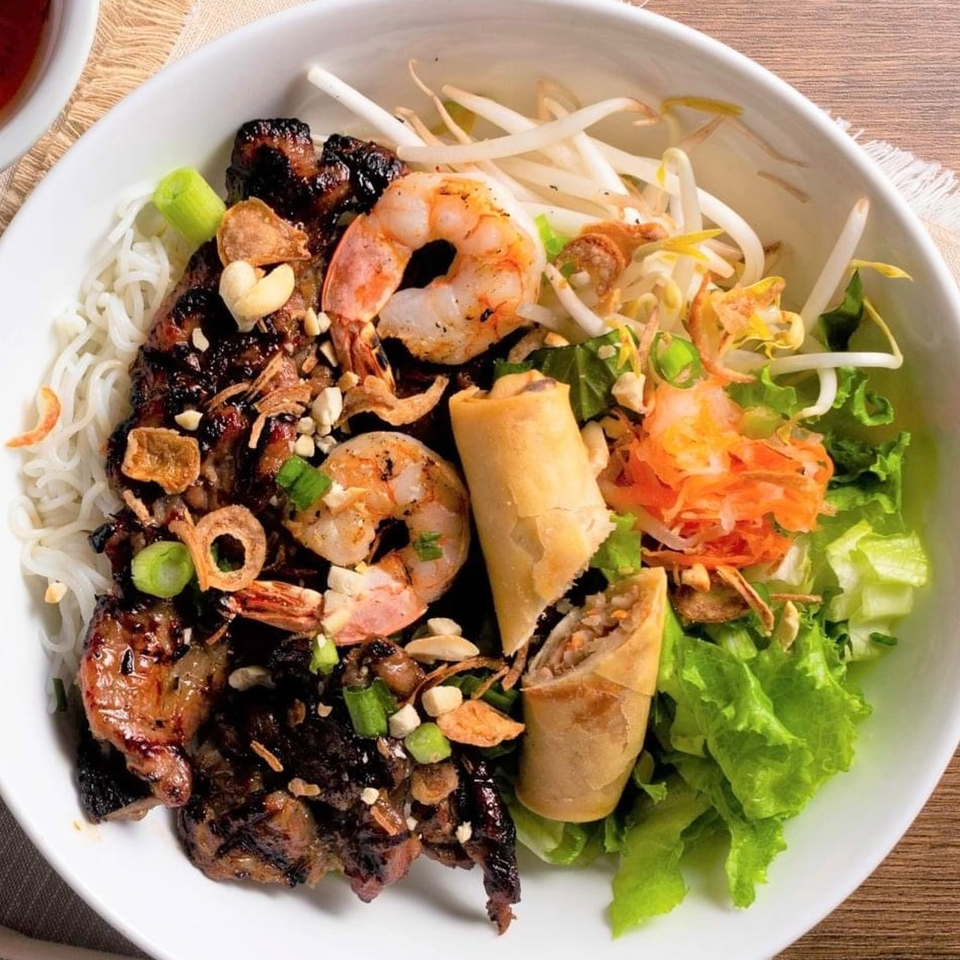 A Vietnamese noodle bowl with grilled pork, shrimp, egg rolls, vermicelli, and fresh vegetables.