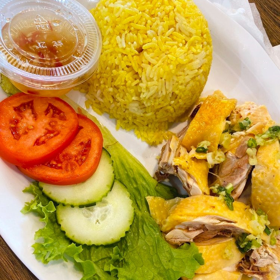 Vietnamese chicken rice with yellow rice, sliced chicken, tomatoes, cucumbers, lettuce, and dipping sauce.